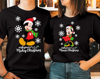 May include: Two black t-shirts featuring Christmas-themed graphics. One shirt displays Mickey Mouse in a Santa hat and scarf with the text "Wish you a Mickey Christmas". The other shirt shows Minnie Mouse in a Santa hat with "Wish you a Minnie Christmas".