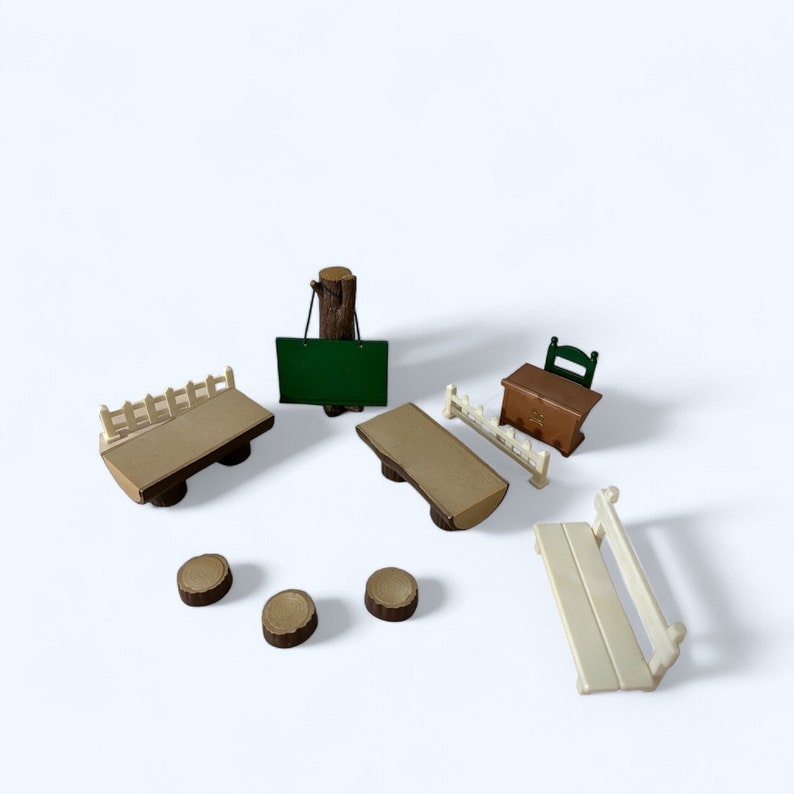 May include: A set of miniature wooden furniture for a dollhouse or playset. The set includes a bench, a table, a desk with a chair, a chalkboard, and three wooden stumps.