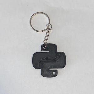 Könnte beinhalten: Ein schwarzer, 3D-gedruckter Python-Logo-Schlüsselanhänger mit einem silbernen Metallschlüsselring.