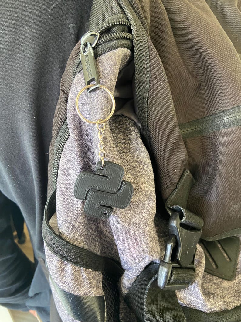 May include: A black Python logo keychain attached to a silver key ring and a black zipper pull on a grey backpack.