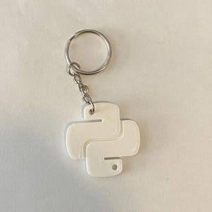 May include: White plastic keychain shaped like the Python programming language logo. The keychain has a silver metal ring and chain.