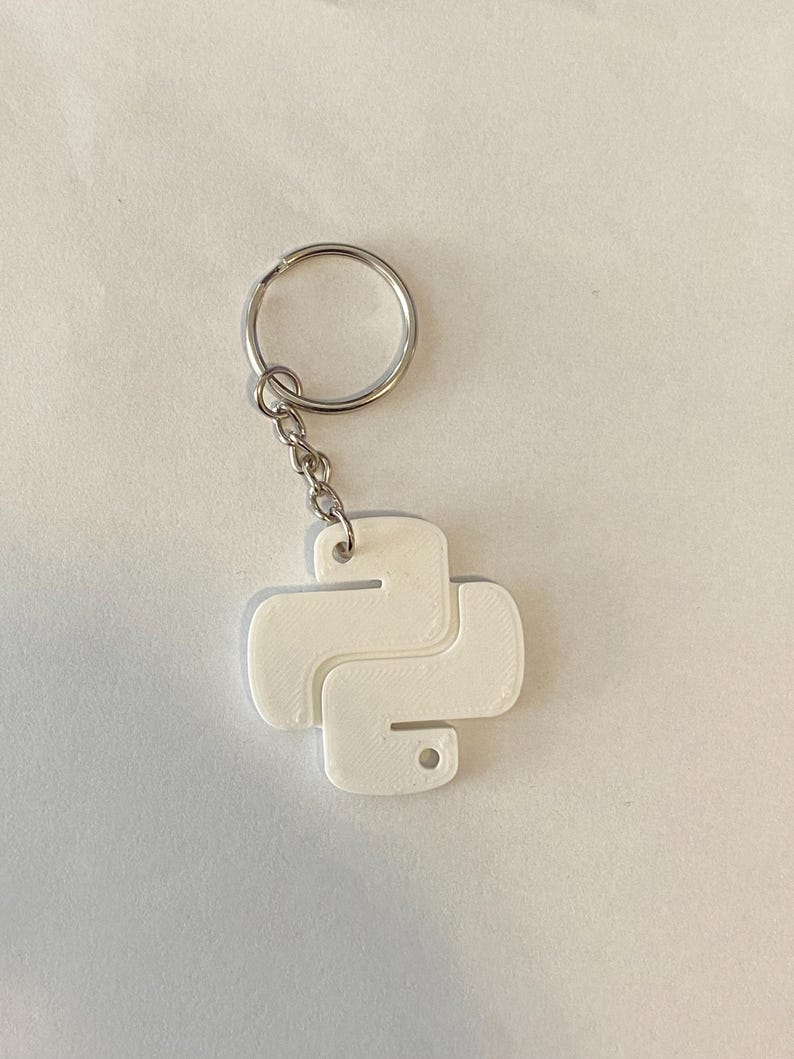May include: White plastic keychain shaped like the Python programming language logo. The keychain has a silver metal ring and chain.