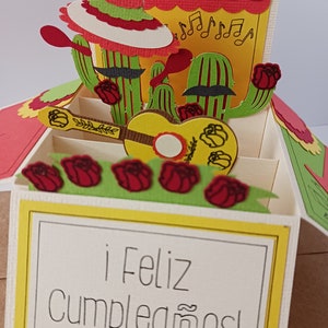 May include: A pop-up card with a yellow, green, and red cactus theme. The card is open and shows a guitar, roses, and the text "&iexcl;Feliz Cumplea&ntilde;os!"