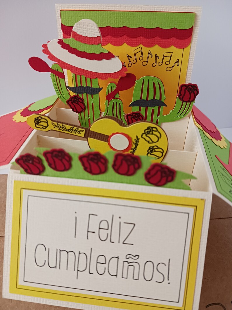 May include: A pop-up card with a yellow, green, and red cactus theme. The card is open and shows a guitar, roses, and the text "&iexcl;Feliz Cumplea&ntilde;os!"