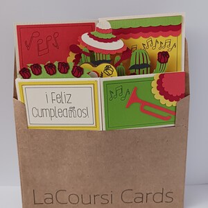 May include: A brown paper envelope with a pop-up card inside. The card features a colorful Mexican fiesta theme with a sombrero, cacti, musical notes, and the text "&iexcl;Feliz Cumplea&ntilde;os!" The envelope has the text "LaCoursi Cards" printed on the front.