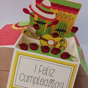 May include: A pop-up card with a yellow, green, and red cactus design. The card has a guitar and a sombrero. The card says "&iexcl;Feliz cumplea&ntilde;os!"