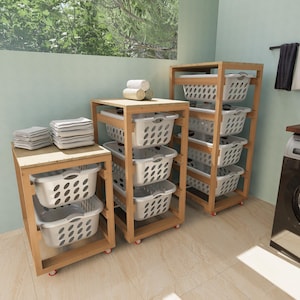 May include: Wooden laundry sorter with three sections, each holding white plastic laundry baskets. The sorter has a light wood finish and red wheels. Stacks of folded towels and rolled towels are on top of the sorters. A washing machine is visible in the background.