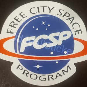 May include: A white sticker with a blue and orange design. The sticker features the text "FREE CITY SPACE PROGRAM" in a circular layout. The center of the design has the letters "FCSP" and a blue planet with stars.