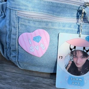 May include: A light blue denim bag with a pink heart-shaped pin that says "I SVT" and a blue diamond graphic. A photo card with a picture of a person and the words "team SVT" is attached to the bag.