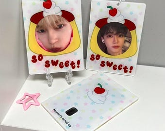 May include: Two white photo card holders with a pudding design and the text "so sweet!"  The photo cards have a clear plastic window to insert a photo. The photo cards are on a white shelf with a pink star-shaped hair clip.