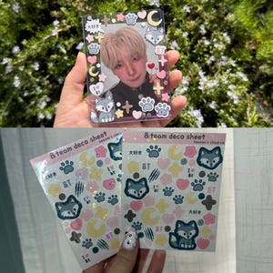 Peut inclure: Un porte-carte en plastique transparent contenant la photo d'une personne, orné d'autocollants représentant des loups, des empreintes de pattes, des cœurs, des étoiles et des lunes. Deux planches d'autocollants &team deco sheet sont présentées.