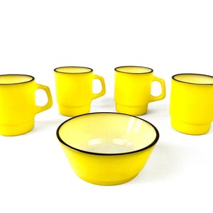 Op de afbeelding: Set van vijf gele keramische mokken met zwarte randen en een gele keramische kom met een zwarte rand.