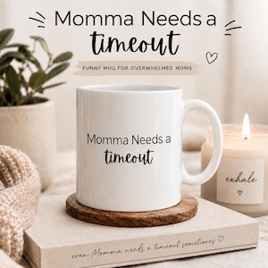 May include: A white ceramic mug featuring the black printed text Momma Needs a timeout. The mug has a cylindrical body and a curved handle. The text is written in a combination of standard sans-serif and cursive fonts on the front of the mug.