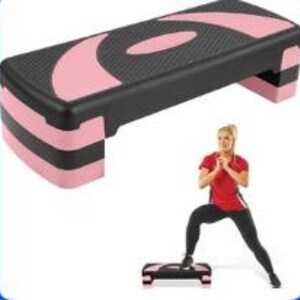 Könnte beinhalten: Schwarze und rosa Aerobic-Step-Plattform. Der Step hat eine strukturierte schwarze Oberfläche mit rosa Akzenten und ist rechteckig, etwa 15 cm hoch. Konzipiert für Fitness-Routinen und Übungen.