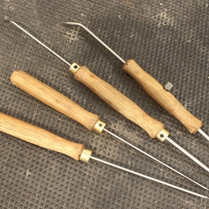 May include: Four wooden handled tools with metal tips. The tools have a brass colored ring near the handle. The tools are on a brown textured surface.