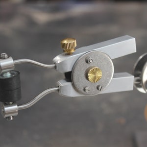 May include: A silver and brass tool with a black rubber roller and a knob. The tool is labeled "HAND MADE".