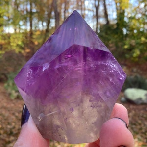 May include: A large, faceted amethyst crystal point with a deep purple colour and a clear, white base. The crystal is shaped like a pyramid and has a smooth, polished surface.