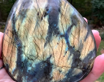May include: A large, smooth, polished labradorite gemstone with a blue, green, and gold iridescent sheen. The stone is shaped like a heart and has a natural, organic look.