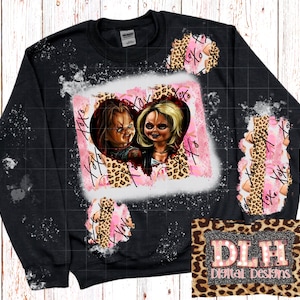 Peut inclure: Sweat-shirt noir avec un motif blanchi représentant un cœur avec un couple de personnages de films d'horreur, un imprimé léopard et les mots "XOXO" en rose. Le sweat-shirt a un aspect vieilli avec des éclaboussures de peinture blanche.