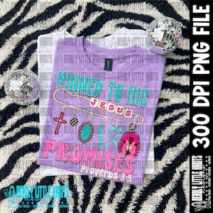 May include: A light purple t-shirt featuring a large safety pin graphic with the text Pinned to His Promises Proverbs 3:5. The design includes charms like a pink cross, a turquoise oval, a blue ribbon, and a pink frame with a cross inside.