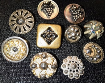 May include: Assortment of ten vintage buttons in various styles and colors. The buttons are made of metal, plastic, and glass. Some buttons feature a black and white design, while others have a gold or silver finish.
