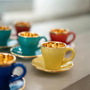 Pode incluir: Um conjunto de xícaras de espresso coloridas e pires com bordas douradas. As xícaras são em tons de azul, verde, amarelo e vermelho.