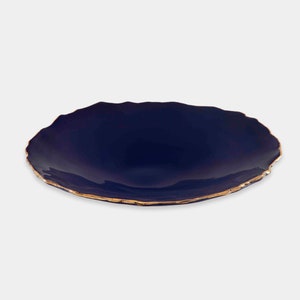 May include: A dark blue ceramic plate with a gold rim. The plate has an irregular, wavy edge.