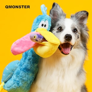 May include: A dog holding a colourful plush toy shaped like a bird. The toy is blue, pink, and yellow. The dog has grey and white fur and is smiling. The text "QMONSTER" is visible in the top left corner.