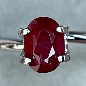 May include: A silver ring with a red oval ruby gemstone.