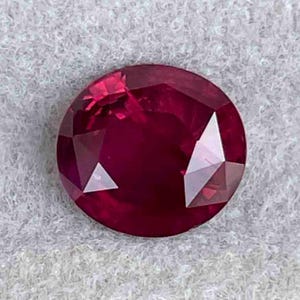 May include: A deep red ruby gemstone with a round cut and many facets.
