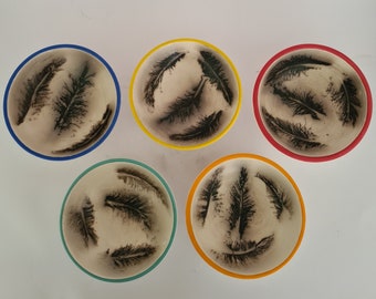 Puede incluir: Cinco cuencos pequeños de cerámica con diseños de plumas negras. Los cuencos son de varios colores: azul, amarillo, rojo, verde y amarillo.