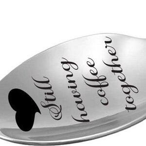 May include: A silver spoon with a black heart and the text "Still having coffee together" engraved on it.