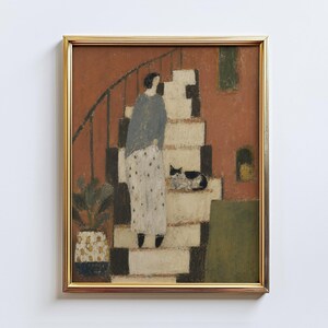 May include: Framed art print featuring a person on a staircase with a black and white cat. The artwork has a warm color palette with a gold frame. A potted plant is visible on the left side of the image.