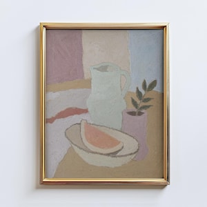 May include: A framed still life painting with a gold frame. The artwork depicts a light green pitcher, a bowl with a slice of watermelon, and a small pink vase with a plant. The background features pastel colors.