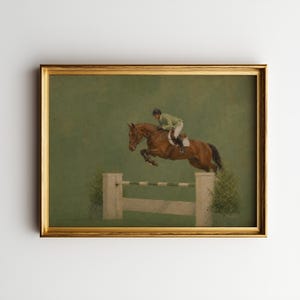 May include: A framed painting depicting a brown horse jumping over a white hurdle with a rider in a green jacket and white breeches. The scene is set against a solid muted green background, capturing the equestrian in mid-air motion.