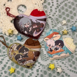 May include: Heart-shaped keychains with anime-style illustrations. One features a character with gray hair and the text "75%". Another has two characters and the text "VANILLA WAFER". The third keychain has two characters and the text "THE DEAD POET AND THE FOOL".