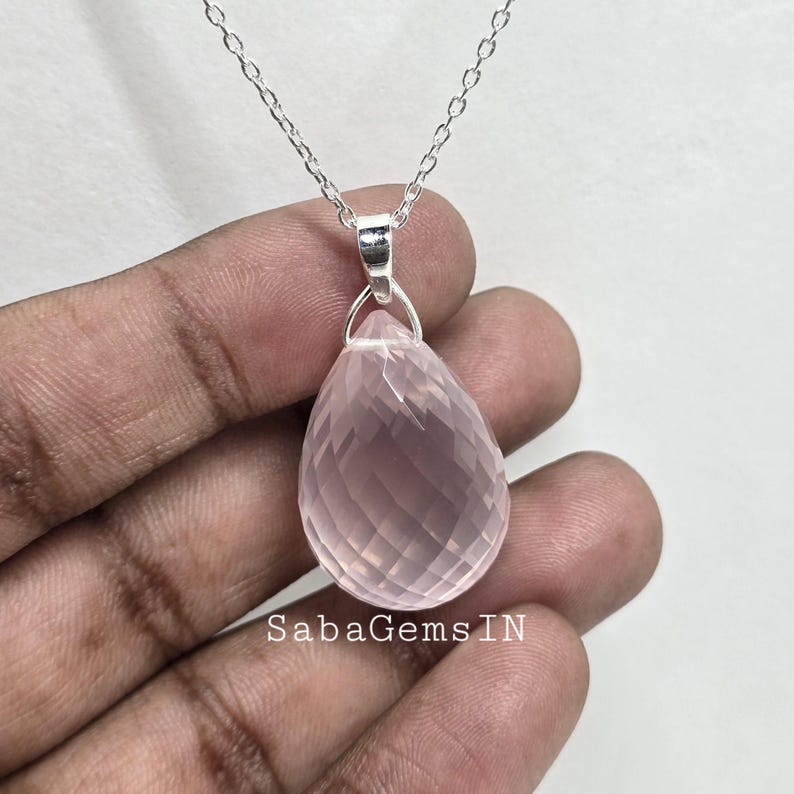 May include: A silver chain necklace with a teardrop-shaped pink quartz pendant. The pendant is faceted and has a translucent appearance.