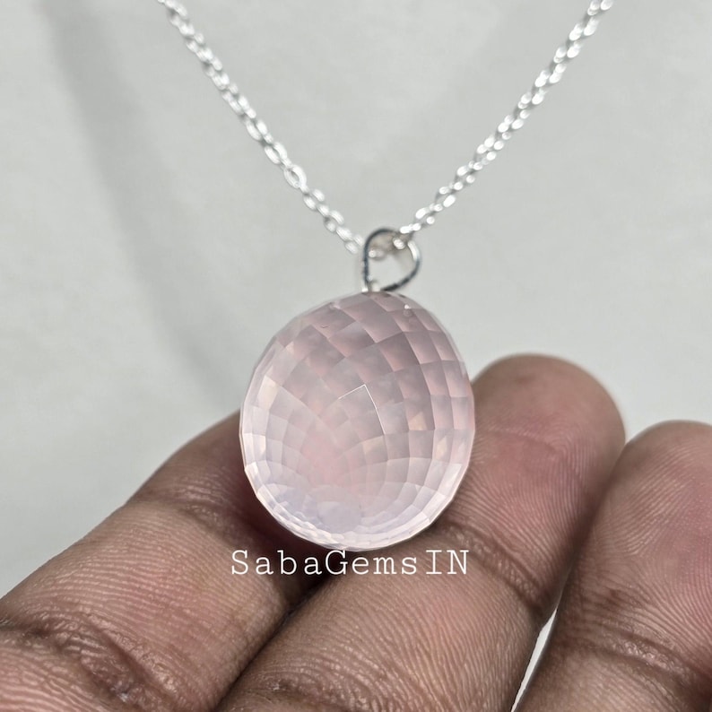 May include: A silver chain necklace with a pale pink rose quartz pendant. The pendant is faceted and has a smooth, polished finish. The text "SabaGemsIN" is visible in the image.