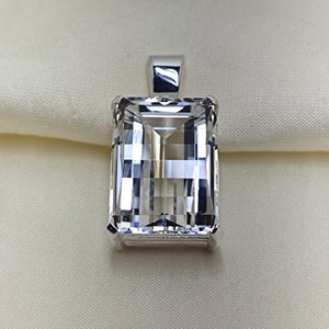 May include: A silver pendant featuring a clear, faceted, rectangular gemstone.