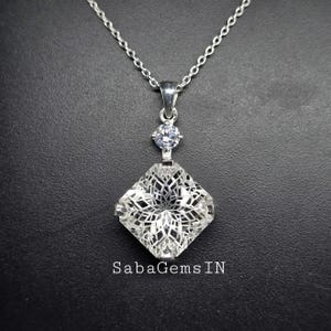 以下が含まれることがあります： クリアなクリスタルがついた、正方形のペンダントが特徴のシルバーチェーンネックレス。ペンダントの上部に、より小さなクリアなクリスタルが取り付けられています。