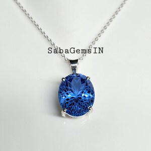 May include: A silver necklace with a large, oval, faceted blue gemstone pendant. The pendant is set in a silver bezel and hangs from a delicate silver chain. The text "SabaGemsIN" is visible.