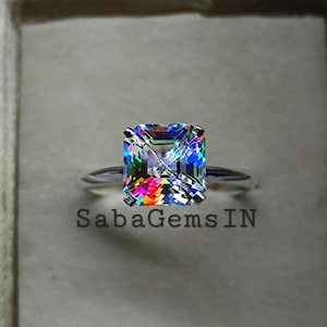 May include: A silver ring featuring a large, square-cut gemstone with a vibrant, multicolored display of light refraction. The text "SabaGemsIN" is visible below the ring.