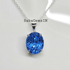 May include: A silver necklace with a large, oval, bright blue pendant. The pendant has a detailed, intricate pattern within the blue gemstone. The text "SabaGemsIN" is visible on the image.