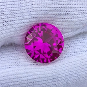 May include: A vibrant pink gemstone with a faceted cut. The gemstone is round and has a high polish.