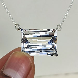 Puede incluir: Un collar de cadena de plata con un gran colgante de cristal rectangular transparente.