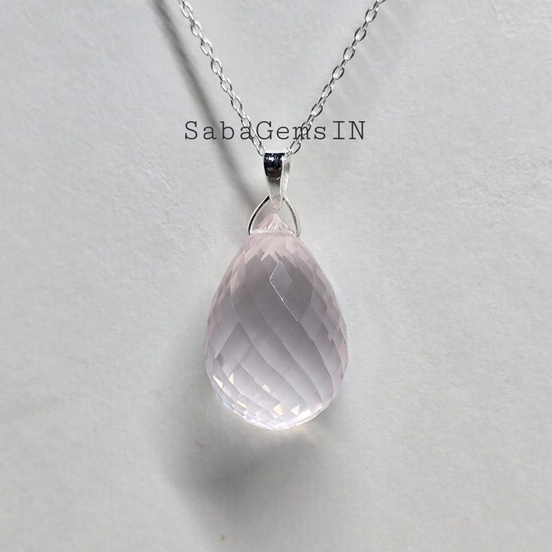 May include: A silver chain necklace with a pink rose quartz pendant. The pendant is faceted and has a teardrop shape.