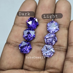 Puede incluir: Seis piedras preciosas de amatista facetadas, tres de color púrpura oscuro y tres de color púrpura claro, dispuestas en dos filas de tres, etiquetadas como "Dark" y "Light" en una mano.