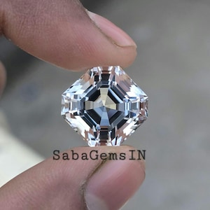 Op de afbeelding: Een heldere, achthoekige geslepen edelsteen met een facetgeslepen ontwerp. De edelsteen wordt in een hand gehouden, de achtergrond is wazig.