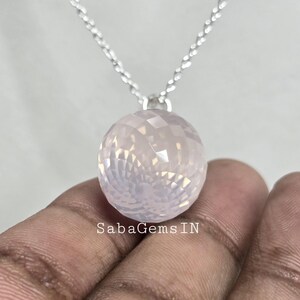 May include: A silver chain necklace with a faceted rose quartz pendant. The pendant is a sphere with a light pink color.