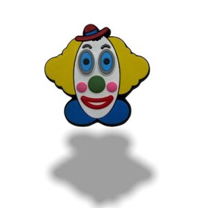 May include: A colourful clown face with a red hat, yellow hair, blue eyes, a green nose, and a red smile. The clown face is made of rubber and is a fun and whimsical decoration.